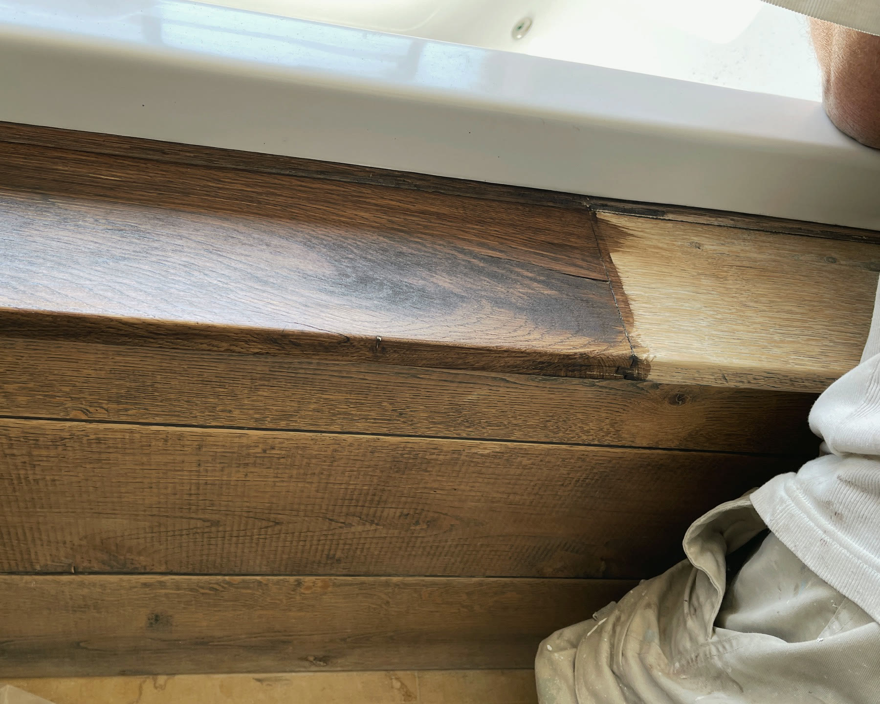 An oak windowsill mid-restoration, freshly repaired wood beside the original stain
